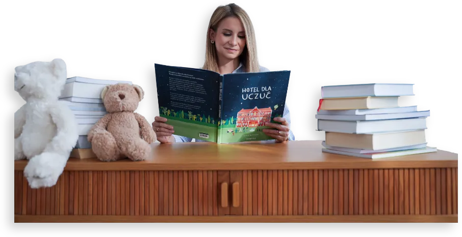 Agata Hemmerling-Goc czyta książkę przy biurku z książkami i pluszowymi misiami